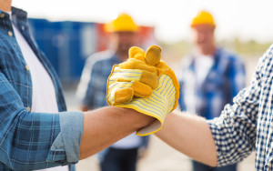 building, teamwork, partnership, gesture and people concept - close up of builders hands in gloves greeting each other with handshake on construction site